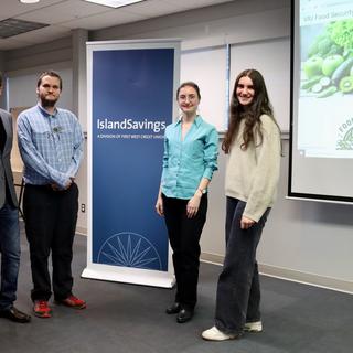 Four students, two males and two females standing beside a banner