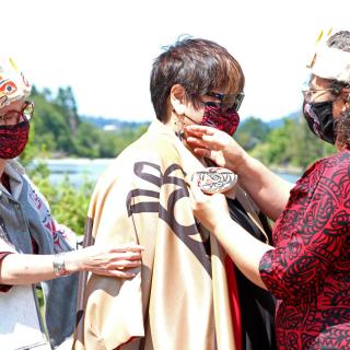 Dr. Judith Sayers is robed by Ay Lelum co-owners, Aunalee and Sophia