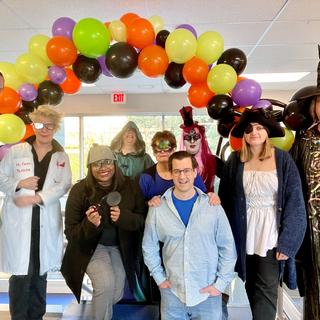 People dressed up for Halloween in an office with a balloon arch behind them. 