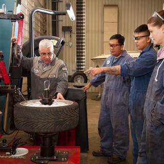 three automotive students receive instruction from a teacher in the shop