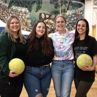 Four students in a gym holding volleyballs