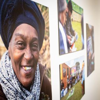 Four photographs hang on the gallery wall. The closest photo is of a person facing the camera smiling.