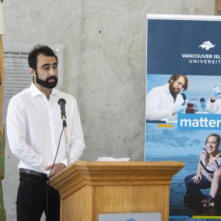 Armin Saatchi, a VIU graduate student, stands at a podium during the BC government funding announcement.