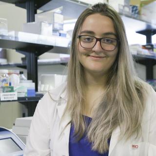 Kimberley Barrett wears a white lab coat and stands in a research lab.