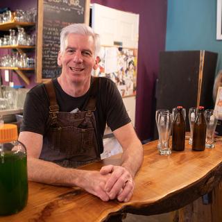 Dave Paul, owner of Love Shack Libations, leans against a wooden counter. Beer bottles and a glass is on his right.