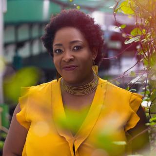 Ozoz Sokoh, wearing a bright yellow shirt, stands in a garden area.