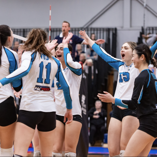 A group of VIU Mariners women's volleyball teammates celebrate in a circle on the volleyball court