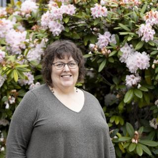 Terri Doughty, a VIU English Professor, smiles while standing in front of a rhododendron plant.