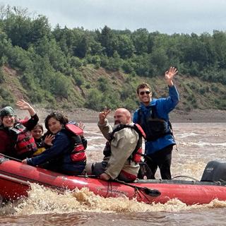 Lucas Gamp in a raft on a river with clients waving at the camera