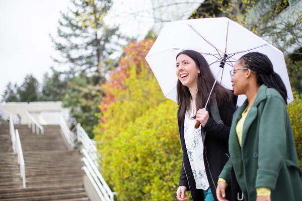 Two students walk near the stairs at VIU, one carries an umbrella