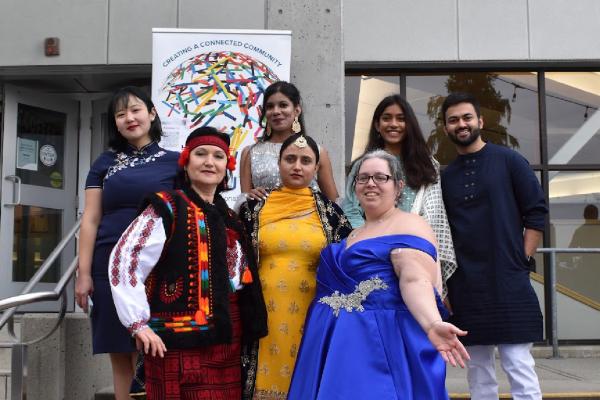 A group of people in various cultural attire standing in front of a WorldVIU sign on the steps of the VIU library