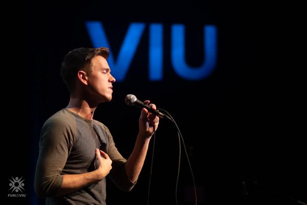 A student sings into a microphone with the VIU logo behind him