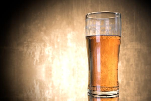 A glass of beer on a table in front of a tan an black background. Image featured in Dr. Marie Hopwood, VIU Department of Anthropology, Archaeology Beer blog