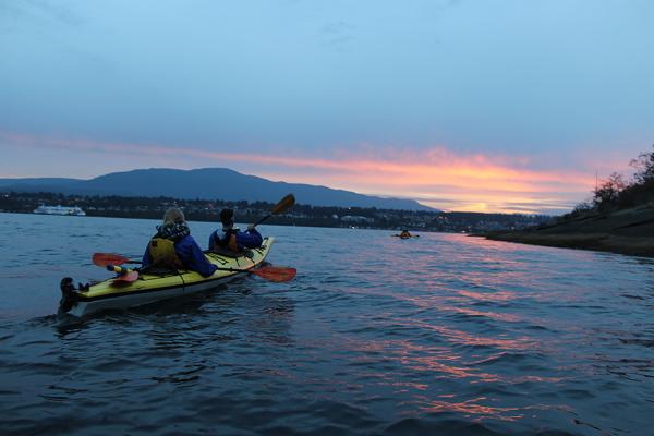 Two people kayaking towards a sunset.