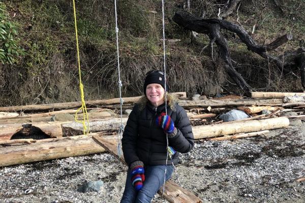 Christin Collishaw sitting outside in a swing at beach and smiling at the camera