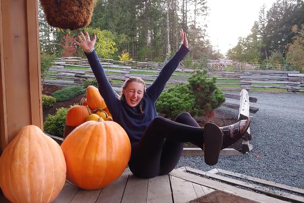 Girl poses with arms spread next to pumpkins