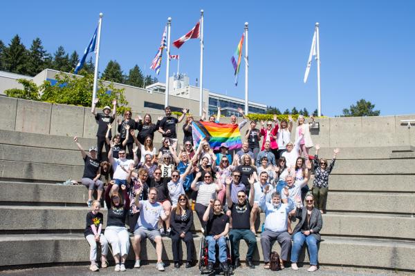 A group wearing Pride t-shirts poses for a photo with the pride flag