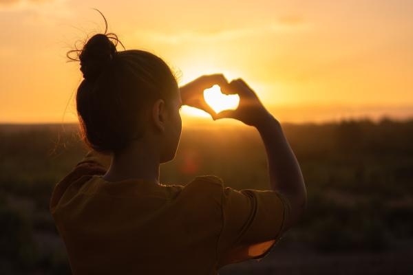 Girl making a heart with her fingers and the sunset poking through