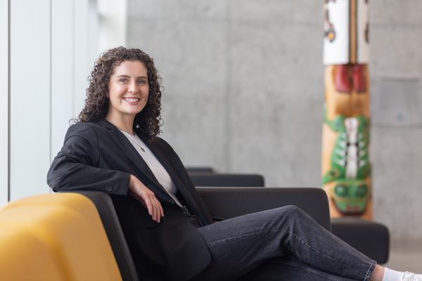 Kayla Passmore sits on a couch in front of the totem in the Centre for Health and Science atrium