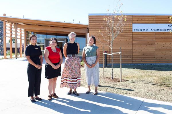 Four people stand in front of Shq'apthut: A Gathering Place