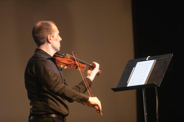 James Mark plays a violin while looking at a stand with sheet music on it.