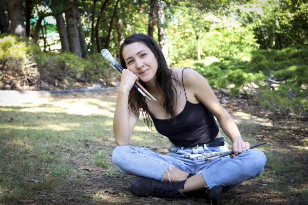 Kashmir Lesnick-Petrovicz sits on the ground and holds paint brushes in her hands.