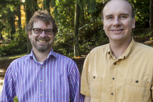 Dr. Erik Krogn and Dr. Chris Gill stand beside each other in a wooded area