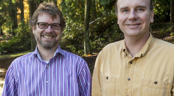 Dr. Erik Krogn and Dr. Chris Gill stand beside each other in a wooded area