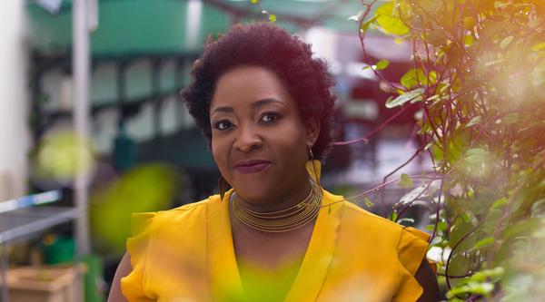 Ozoz Sokoh, wearing a bright yellow shirt, stands in a garden area.