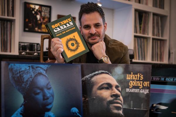 Paul Watkins holds up a copy of his new book in his right hand while resting his chin on the other.