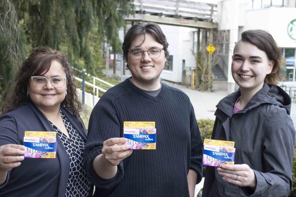 Three people hold up tampon boxes