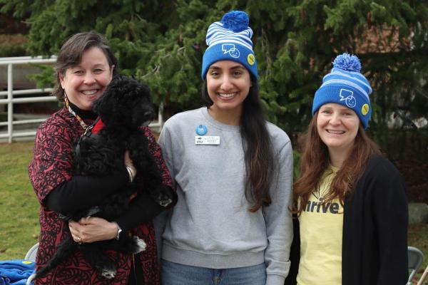 Three people pose, one of whom is holding a dog