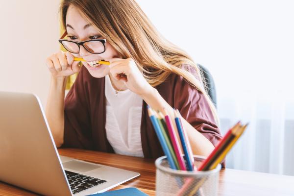 Girl sitting looking at laptop and biting a pencil