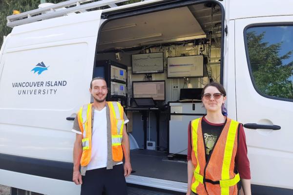 Trevor Michalchuk and Lily Eggert, wearing high visibility vests, while standing in front of the Mass Specmobile.