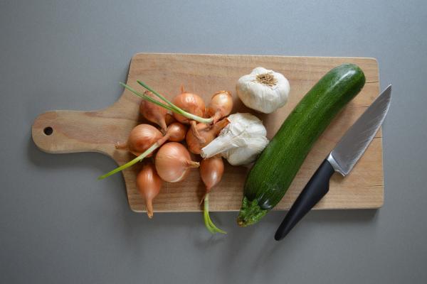 A cutting board with onions, garlic and zucchini