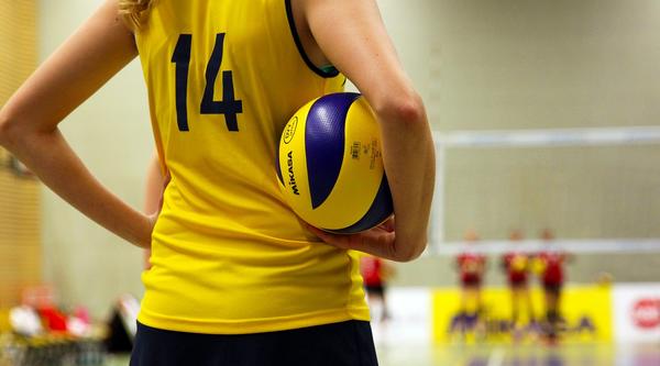 A volleyball player holds a ball, other volleyball players can be seen in the background