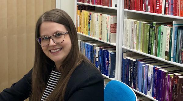 Dr. Whitney Wood sits at a desk with a shelf of books behind her.