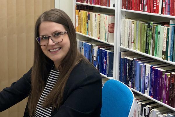 Dr. Whitney Wood sits at a desk with a shelf of books behind her.