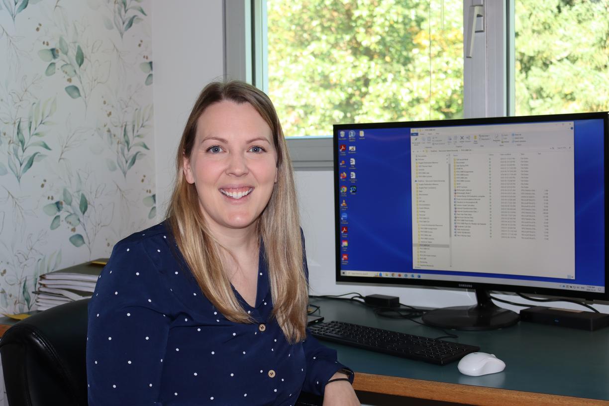 VIU Psychology Professor Becky Earhart sitting at her desk in front of a computer screen and smiling at the camera.