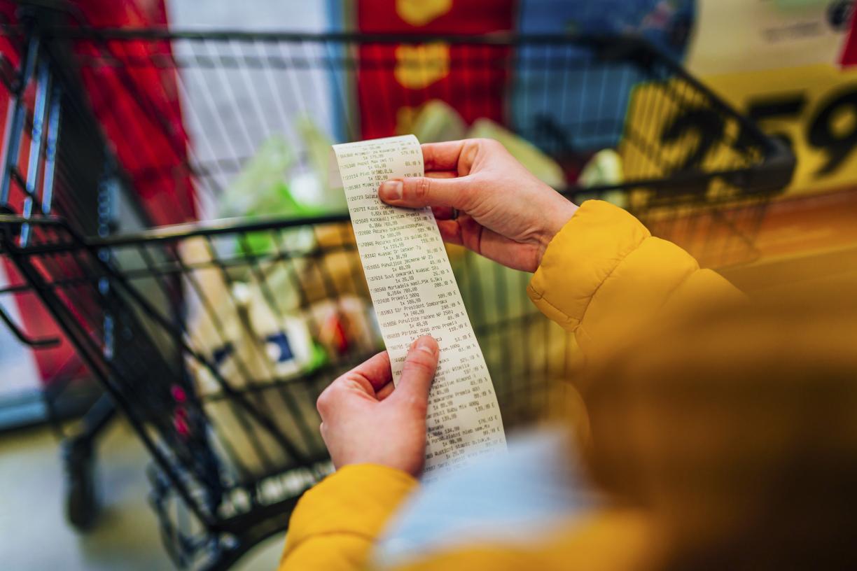 Hands hold a long bill with a grocery cart in the background