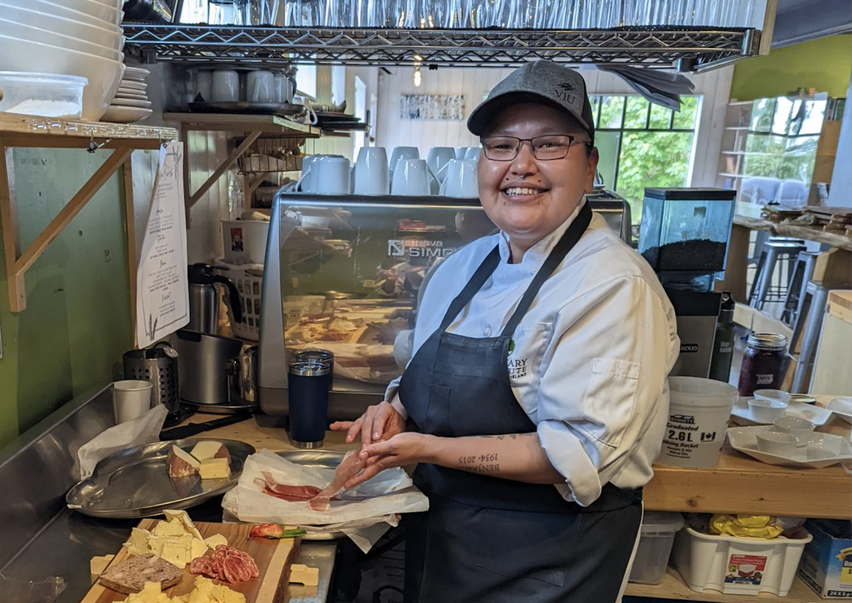 VIU Culinary Arts student Darlene Charlie making a sandwich in the Birch Tree cafe kitchen and smiling at the camera