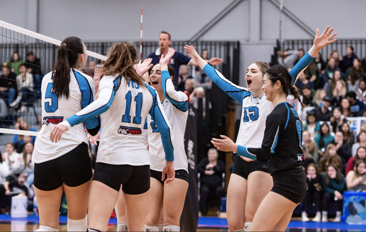 A group of VIU Mariners women's volleyball teammates celebrate in a circle on the volleyball court