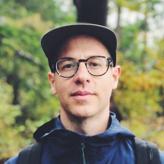 Sebastian Abboud stands in front of some trees while wearing a hat and raincoat.