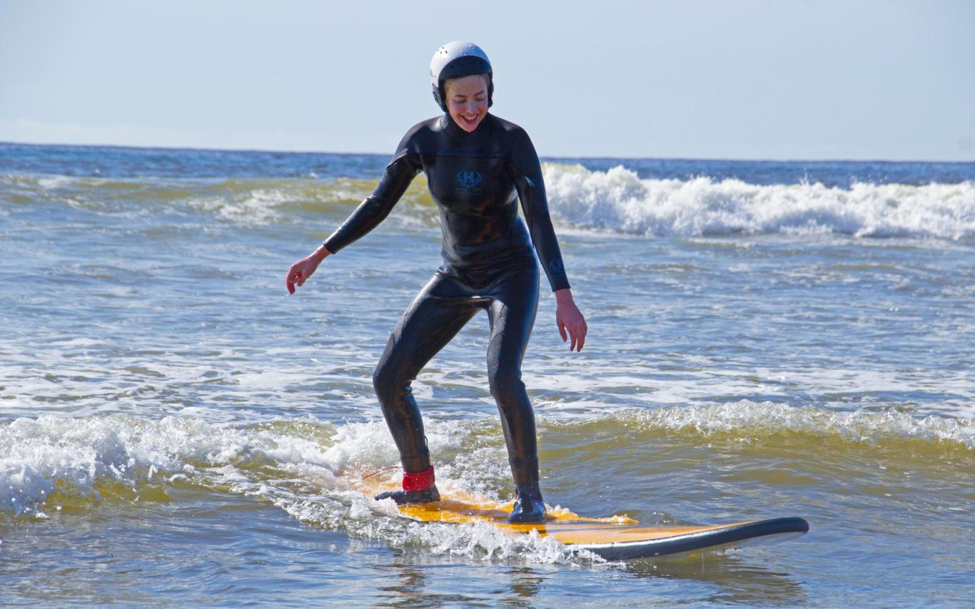 A woman wearing a wetsuit stands up on a surfboard